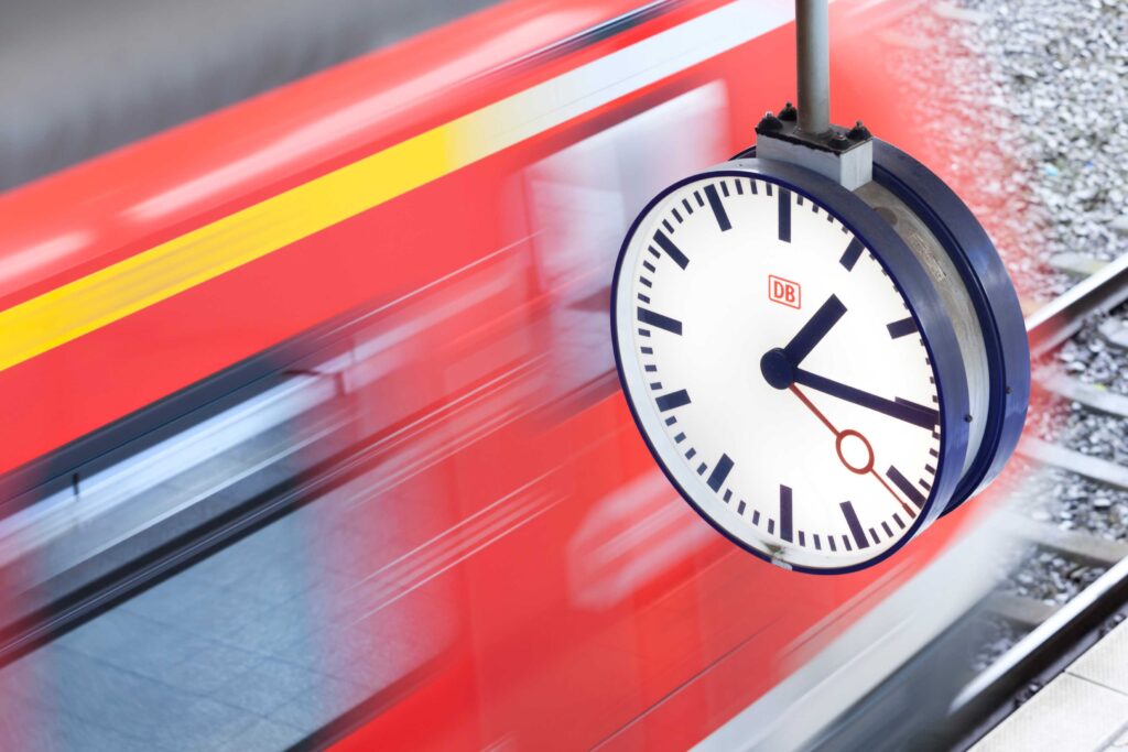 Eine Bahnhofsuhr hinter der ein Zug vorbeifährt.